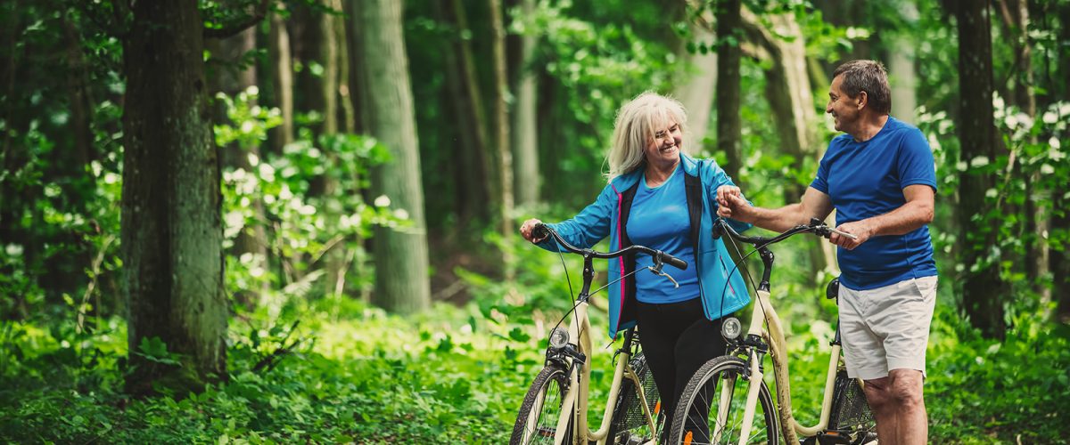 Retired couple walking with bikes in the forest. Active elderly people. Leisure activities.